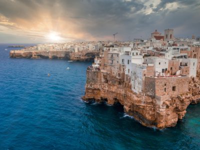 A cityscape of Polignano a Mare surrounded by the sea under the sunlight and a cloudy sky in Italy